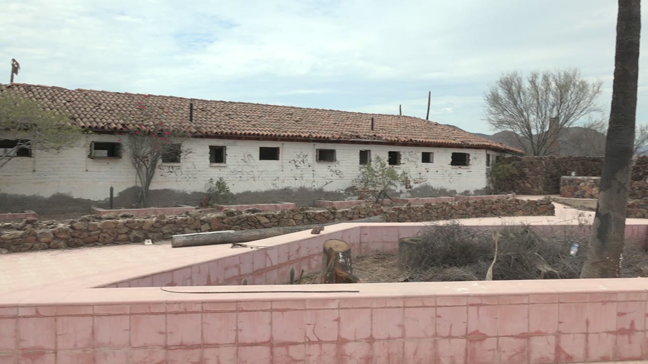 In Mulege, Baja California Sur, the pink tiled wall fills the foreground while the white building and red roof run across the background, with the roof worker still visible high in frame.