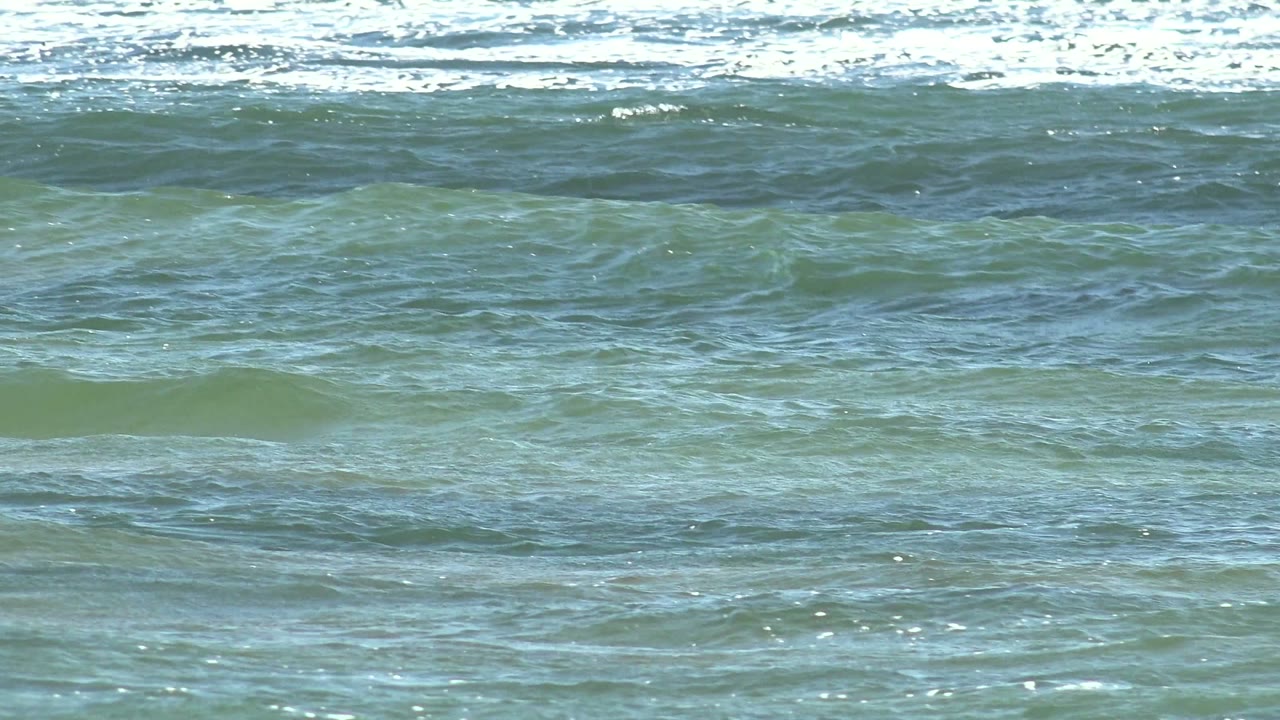 Blue-green ocean water at La Bocana, Baja California Sur, with a bright band of breaking white surf near the top and no visible people.
