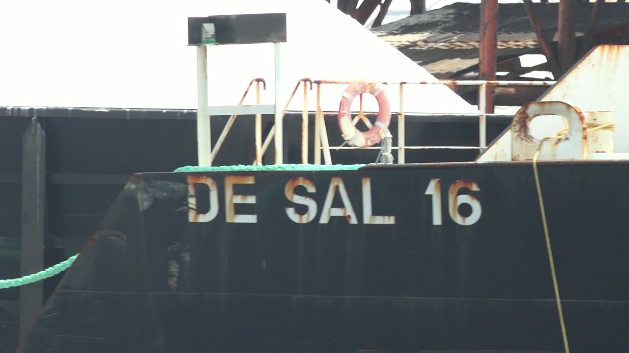 DE SAL 16 lettering on a black barge with railing, life ring, and rusted structure.