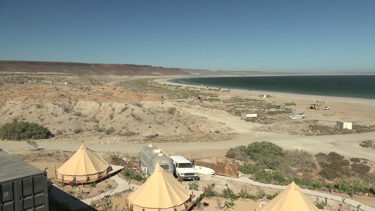 Campsite tents and white van below a sandy beach and blue water.