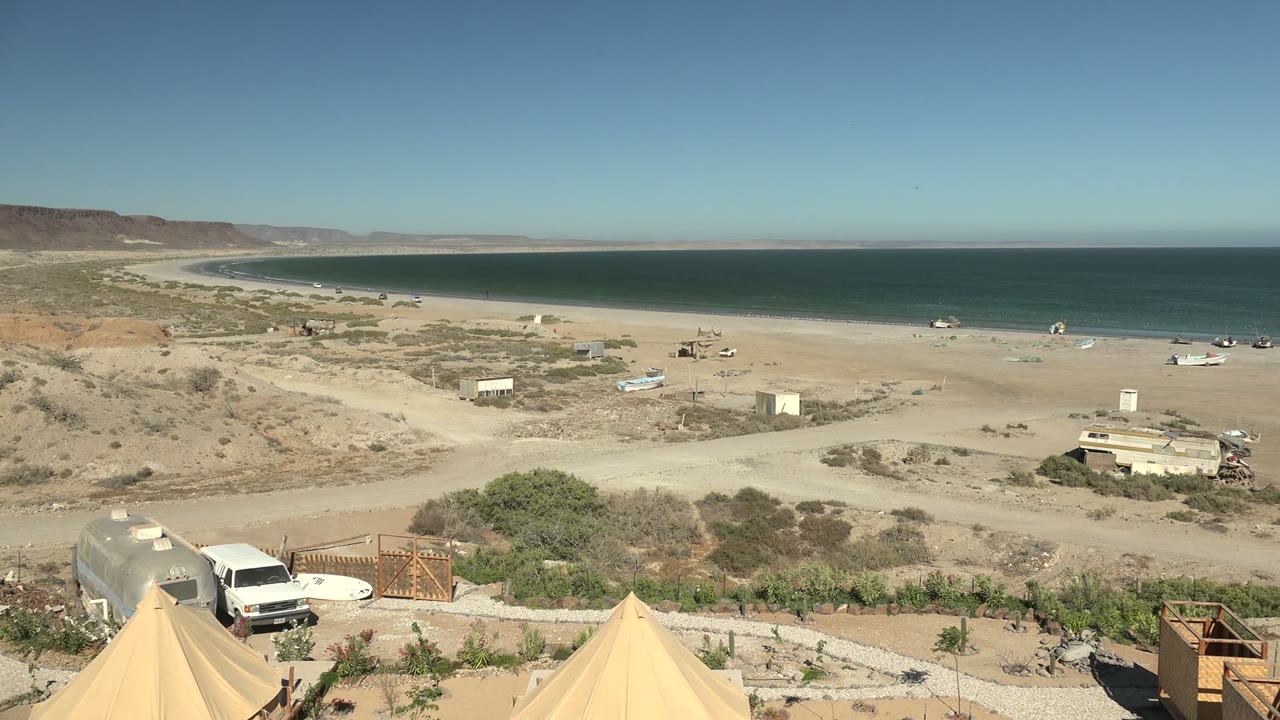 Raised view of desert shore with tents, van, small structures, and blue ocean