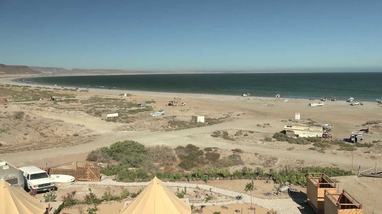 Oceanfront desert beach with tents partly leaving frame and small structures inland