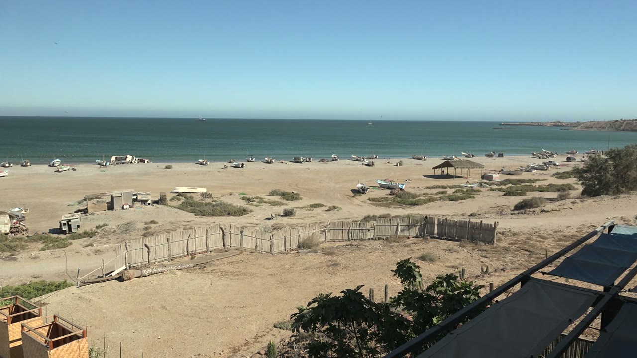 Sandy shore with scattered boats, fence, and clear ocean horizon