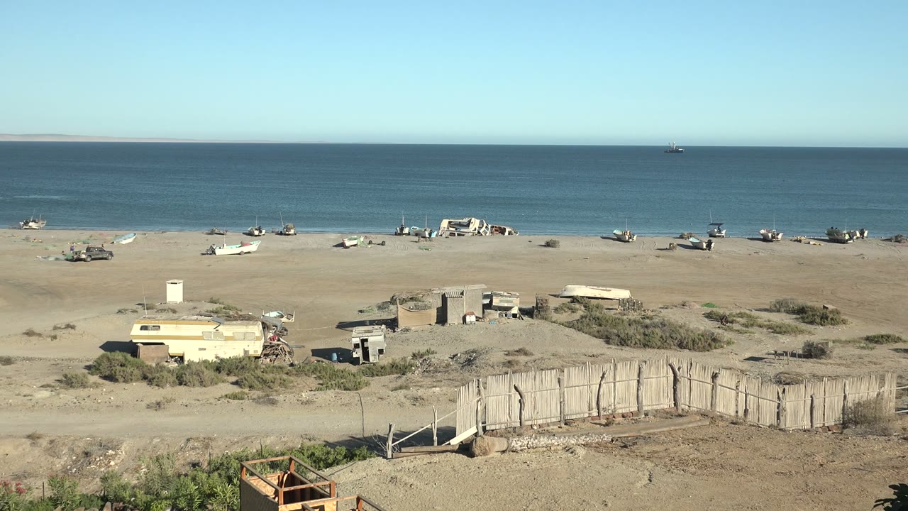 Abandoned boats line a sandy shore below a clear blue sky and calm sea.