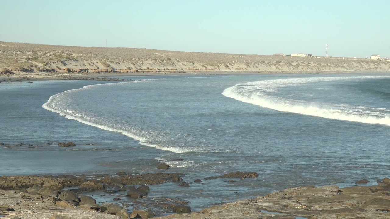 White foam spreads across blue water beside foreground rocks.