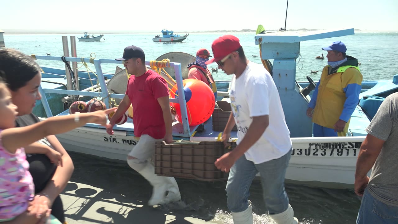 Woman holding a child near fishermen and a docked boat.