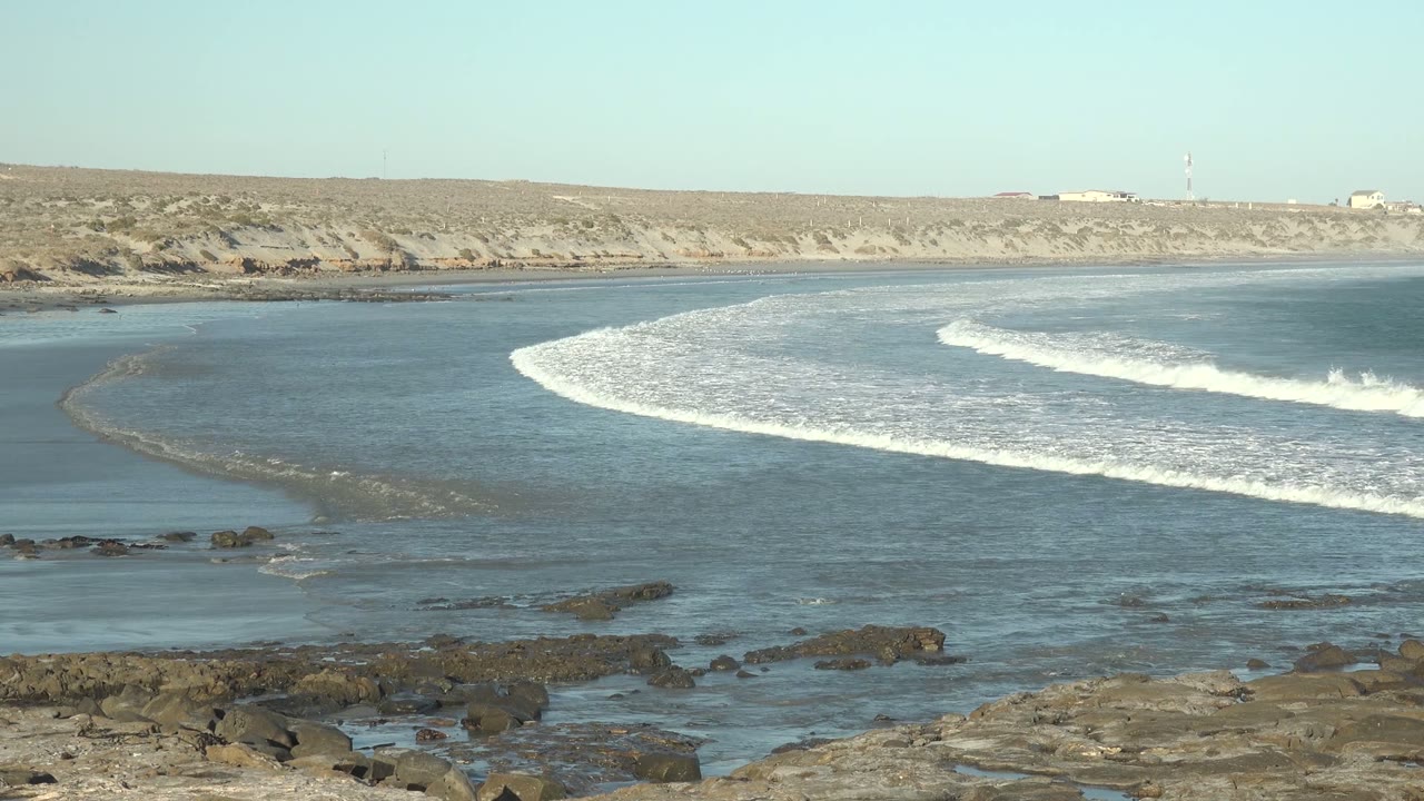 White foam bands advance across shallow coastal water near rocks.