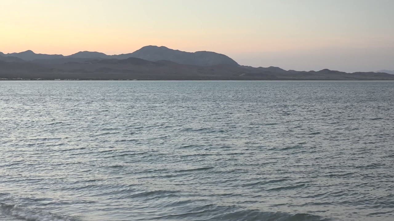 Gentle water surface with mountains under fading sky
