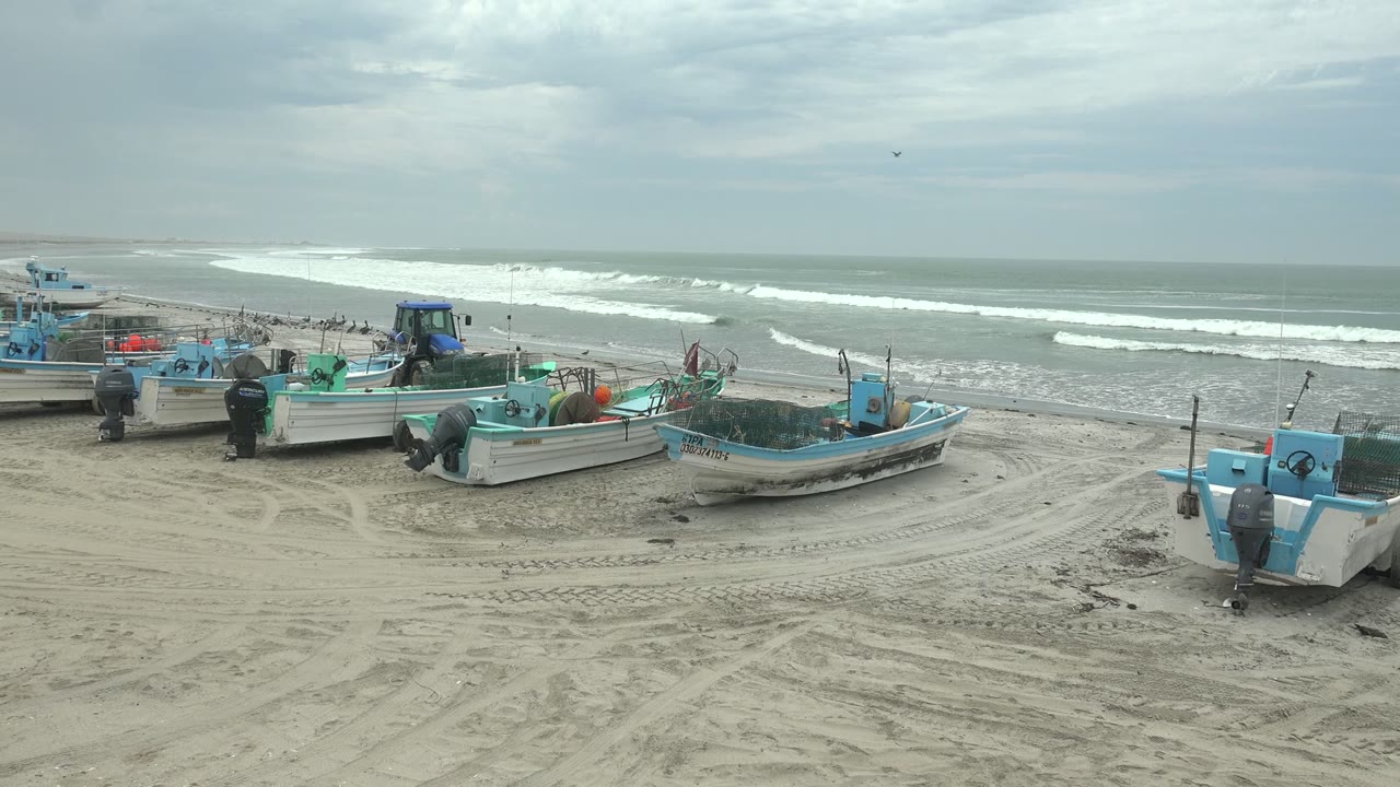 Several small fishing boats sit across the sandy Punta Abreojos shoreline, with pale surf bands moving in the background and no visible people in the frame.