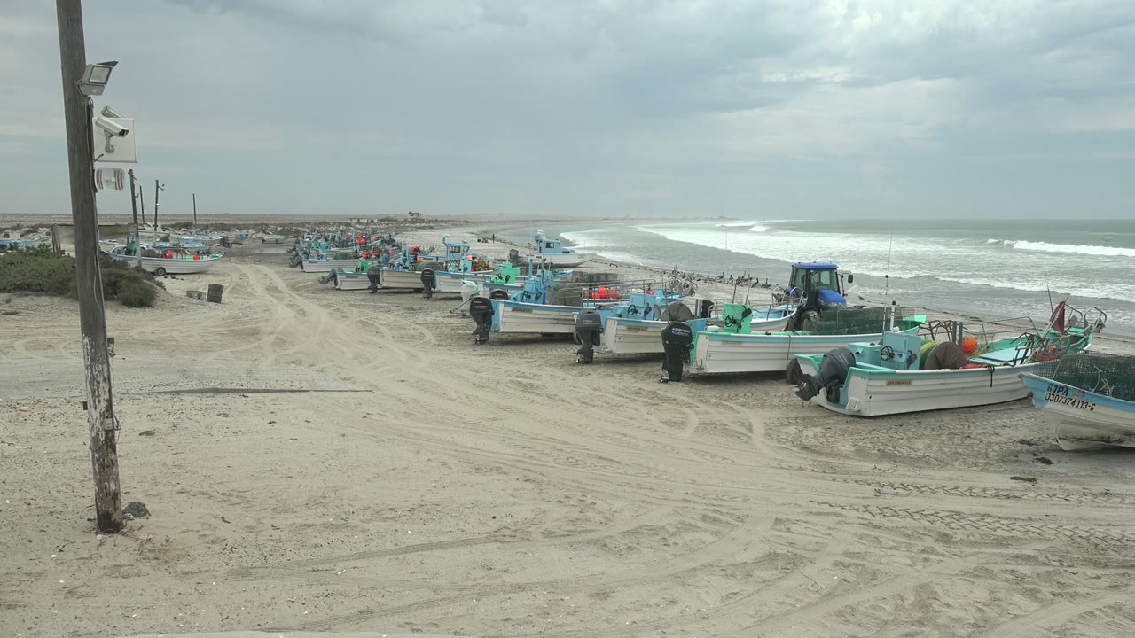 Rows of fishing boats on sand with people working near the shoreline.