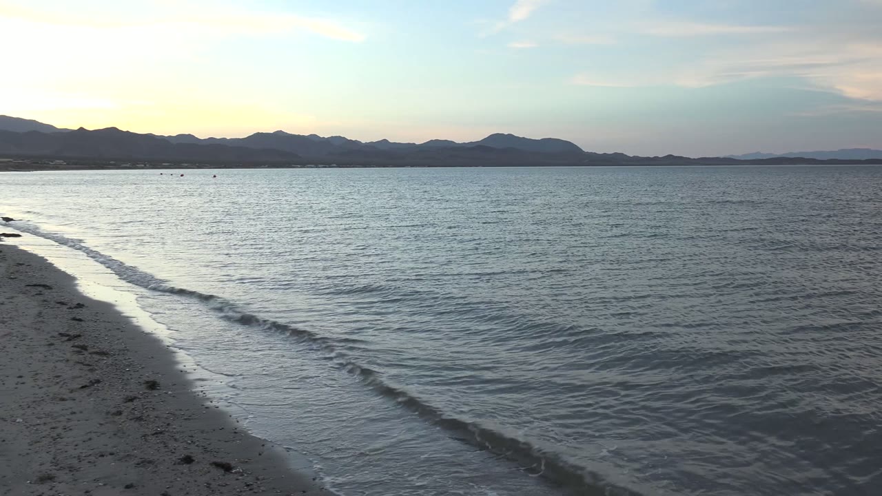 Wave line sliding along wet sand with mountains across the water