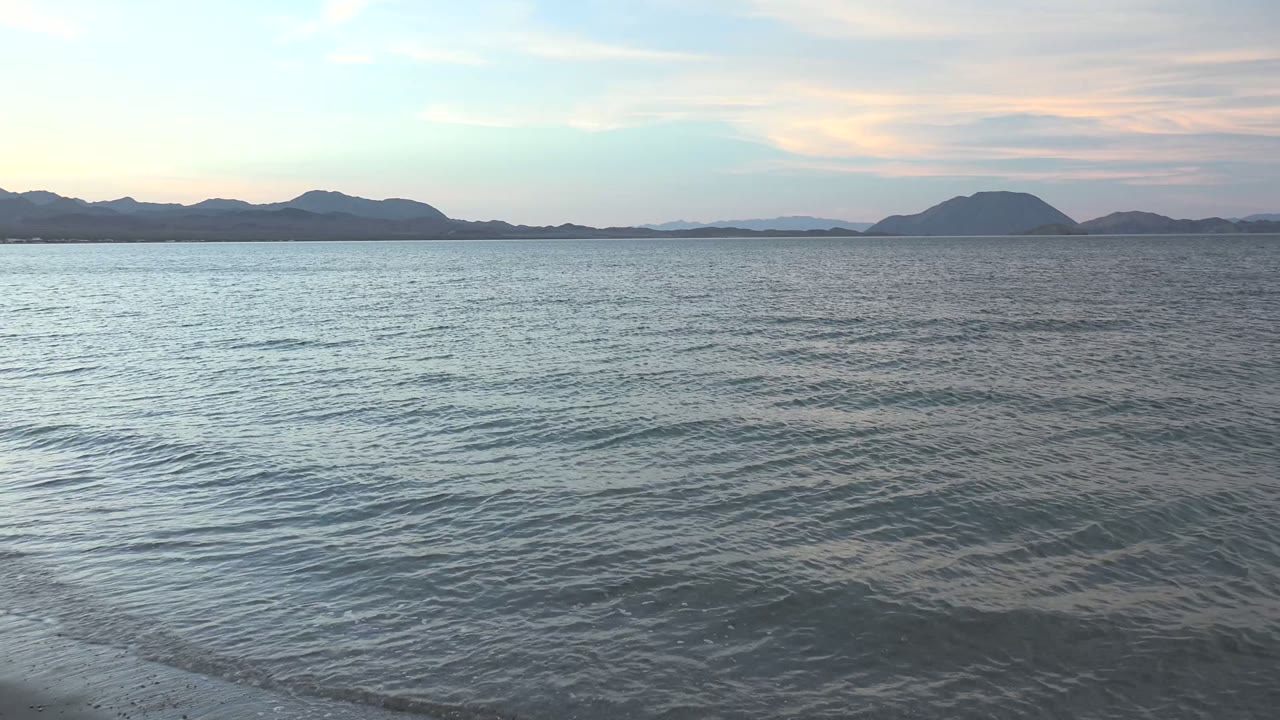 Rippling ocean surface with low dark islands under pastel clouds.