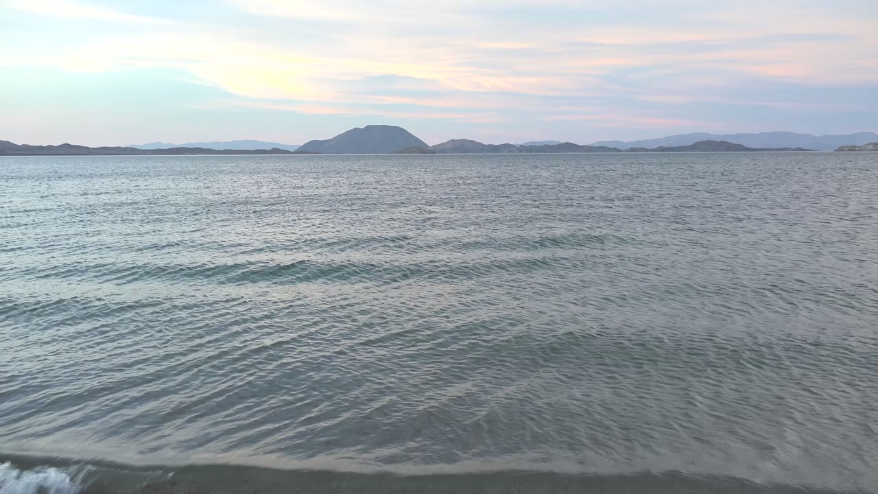 Rippled sea water at Bahia De Los Angeles shows a small breaking wave near the lower frame, distant islands on the horizon, and no visible people.