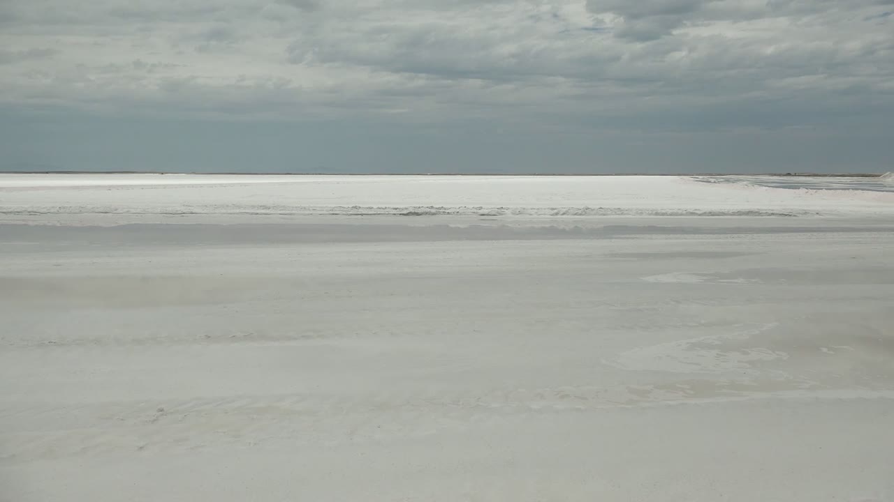 A flat frozen river surface fills the foreground in Guerrero Negro, while layered gray clouds sit above the pale horizon and no people are visible.