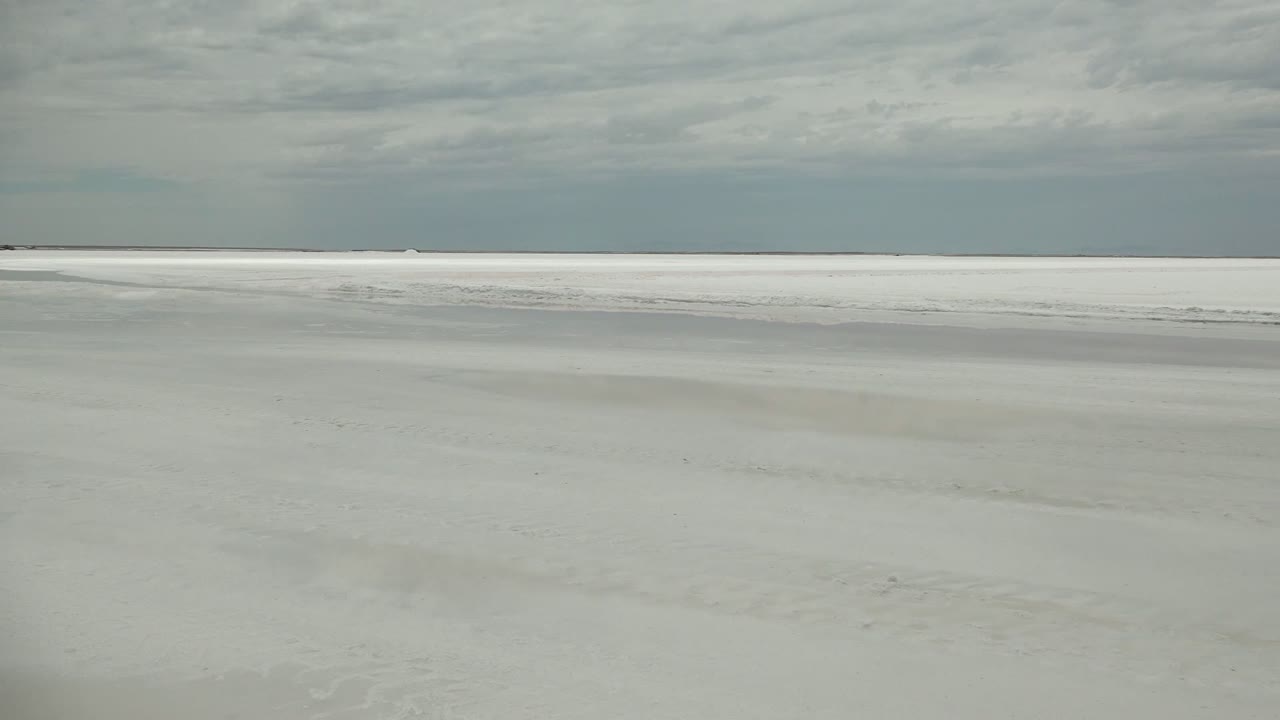 Pale flat ground fills the lower frame in Guerrero Negro while a long gray cloud band hangs above the distant white horizon, with no visible people.