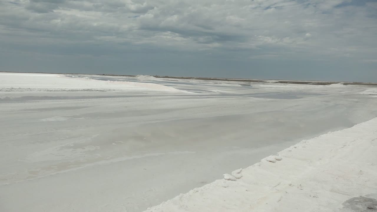 Pale icy waterway and snow ridge below a clouded sky