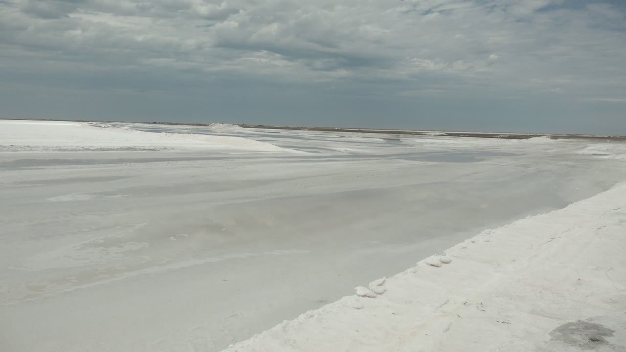 White snow banks edge a broad frozen channel in Guerrero Negro, Baja California Sur, Mexico, with a muted gray sky and no visible people.