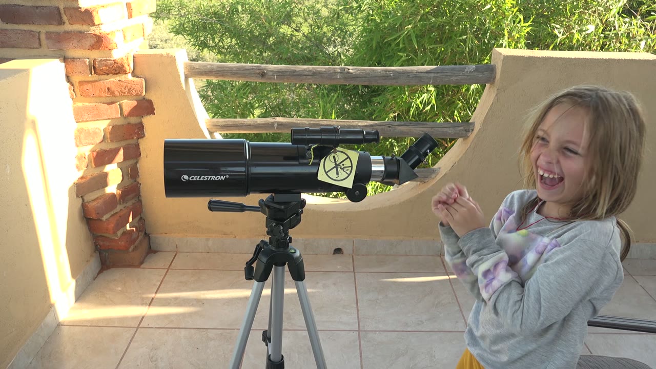 Child laughing near a telescope on a tiled patio.