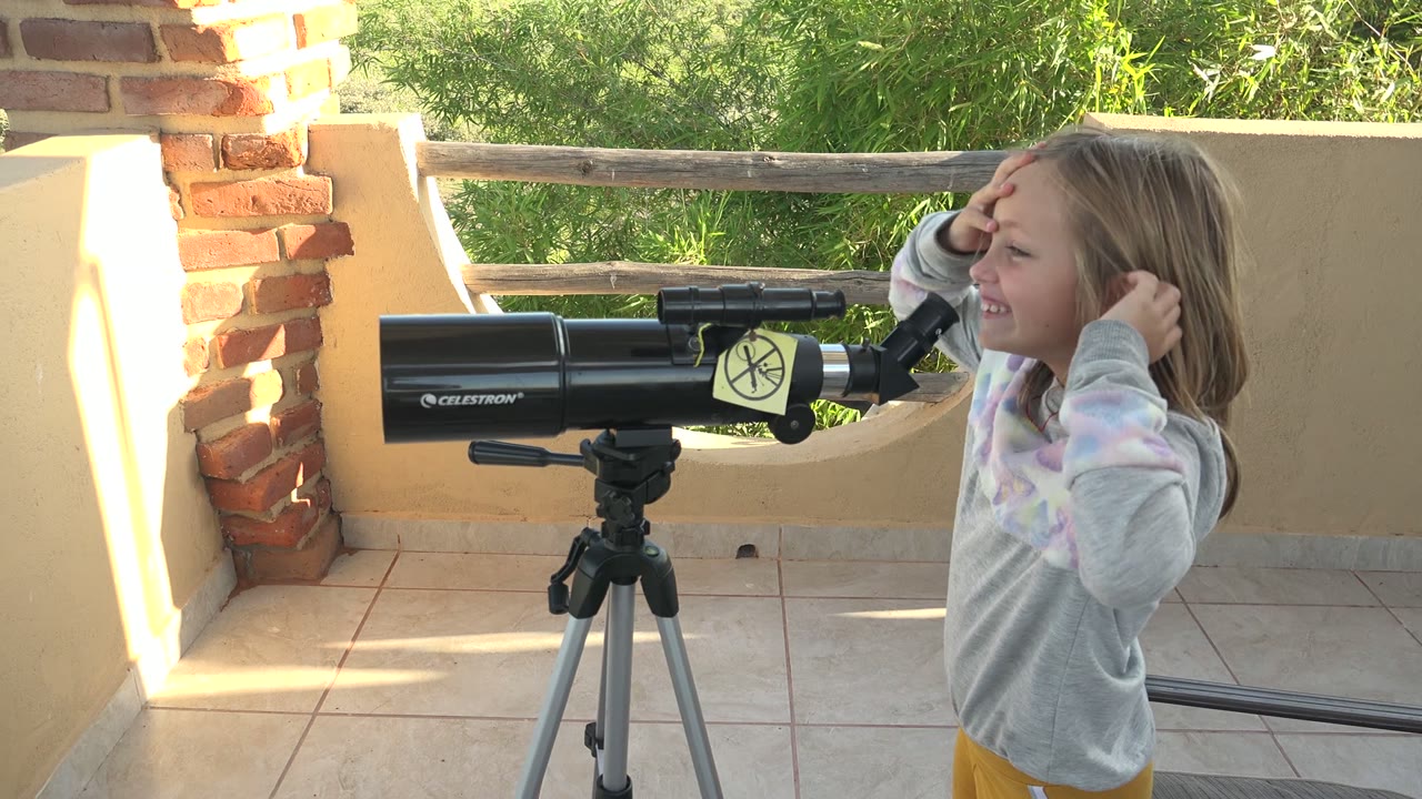 Girl smiling beside a telescope after adjusting her hair.