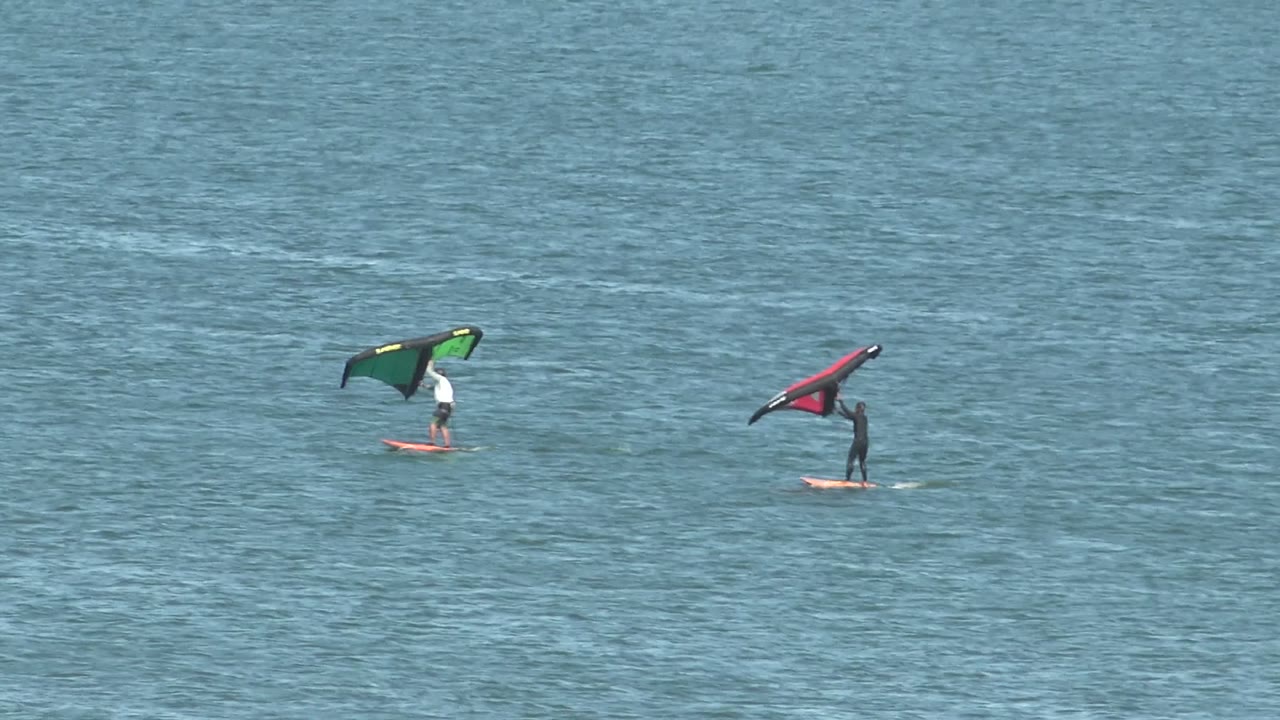Two kite surfers continue across rippled ocean water.