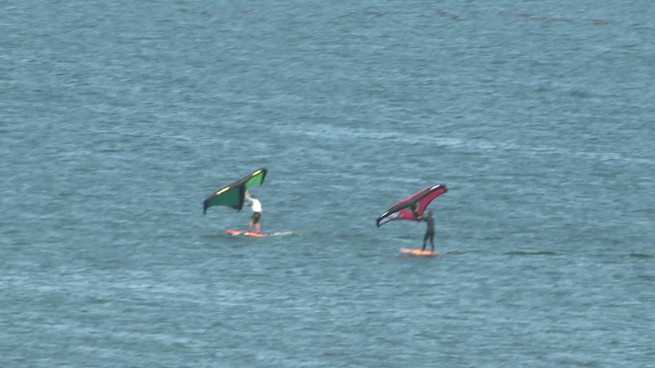 Two distant kite surfers ride on calm blue water in San Juanico, Baja California Sur, with the green kite to the left and the red kite to the right.