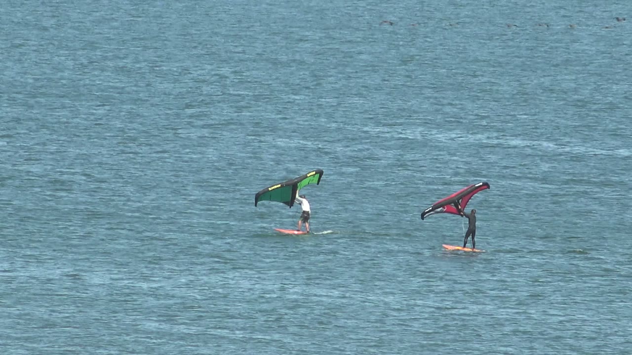 Two kite surfers continue across calm blue ocean water.