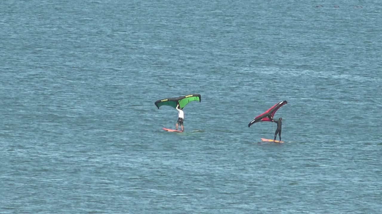 Both kite surfers glide over the open blue water at San Juanico, with the green kite rider on the left and the red kite rider on the right.