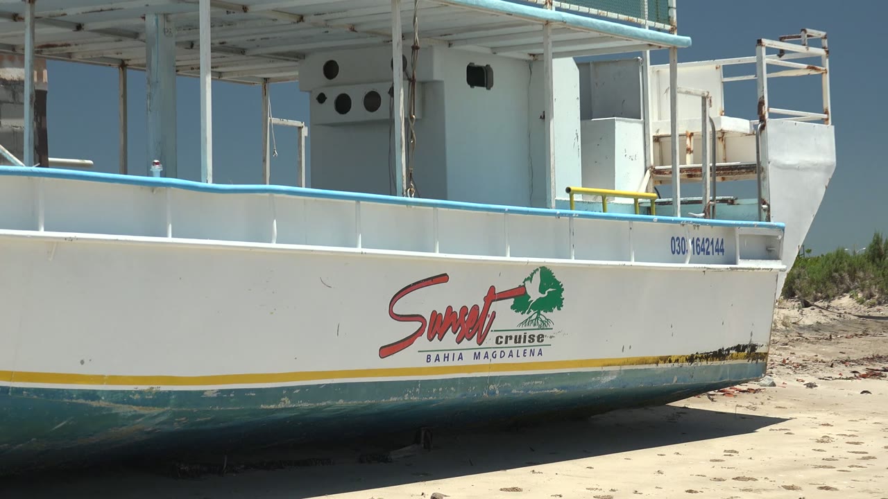 Boat hull with Sunset Cruise logo and beach sand behind it.