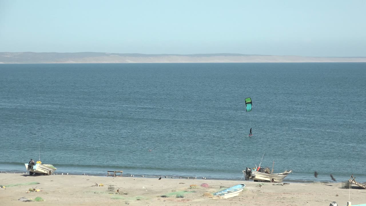 Kitesurfer offshore with green kite and boats along the beach.
