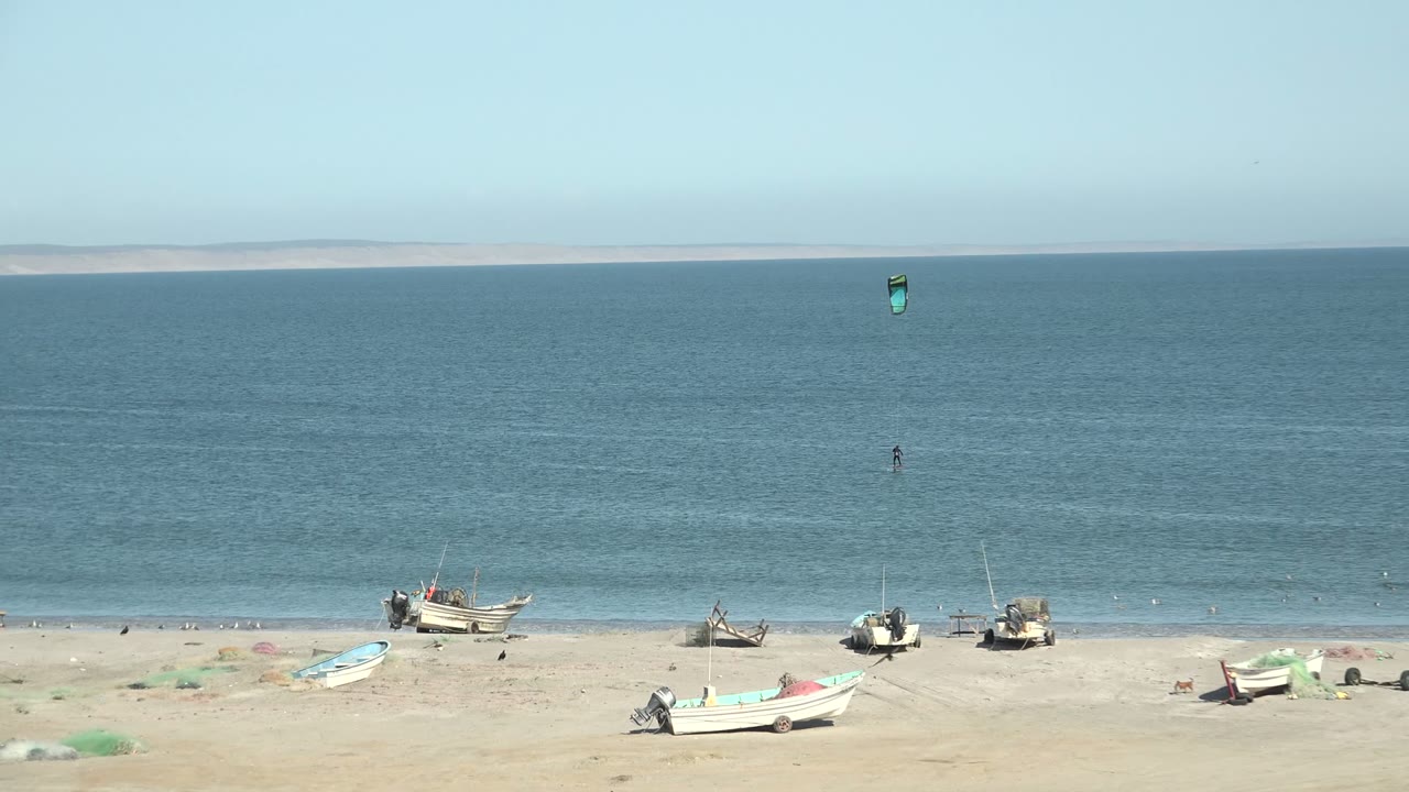 Beach boats beneath a clear sky with kite surfer offshore