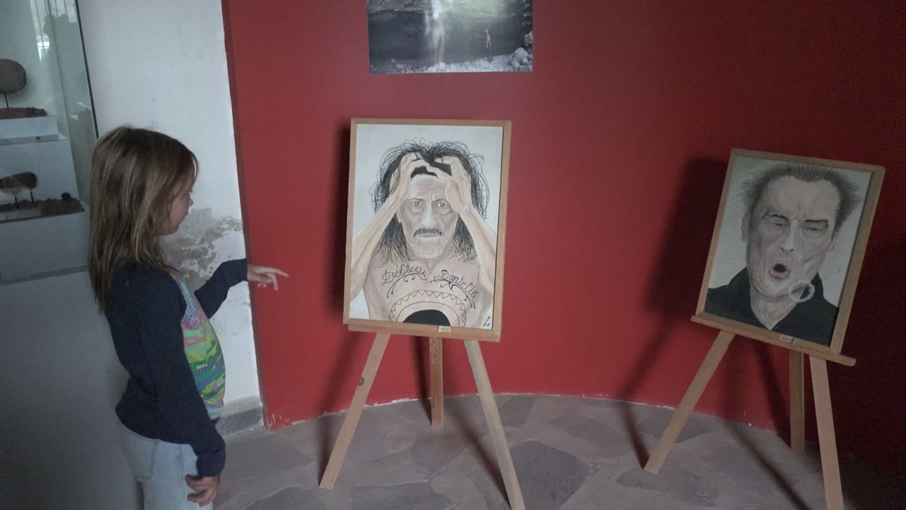 A similar gallery view shows the girl still pointing from the left, with the two framed drawings spaced across the red wall behind her gesture.