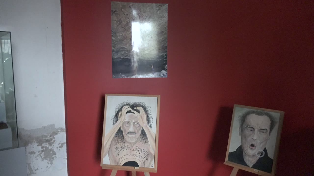 Two portrait paintings on wooden easels below a reflective artwork on a red wall.