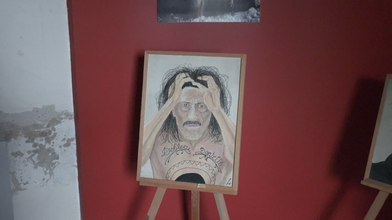 Central portrait painting on an easel with red wall and white peeling wall beside it.