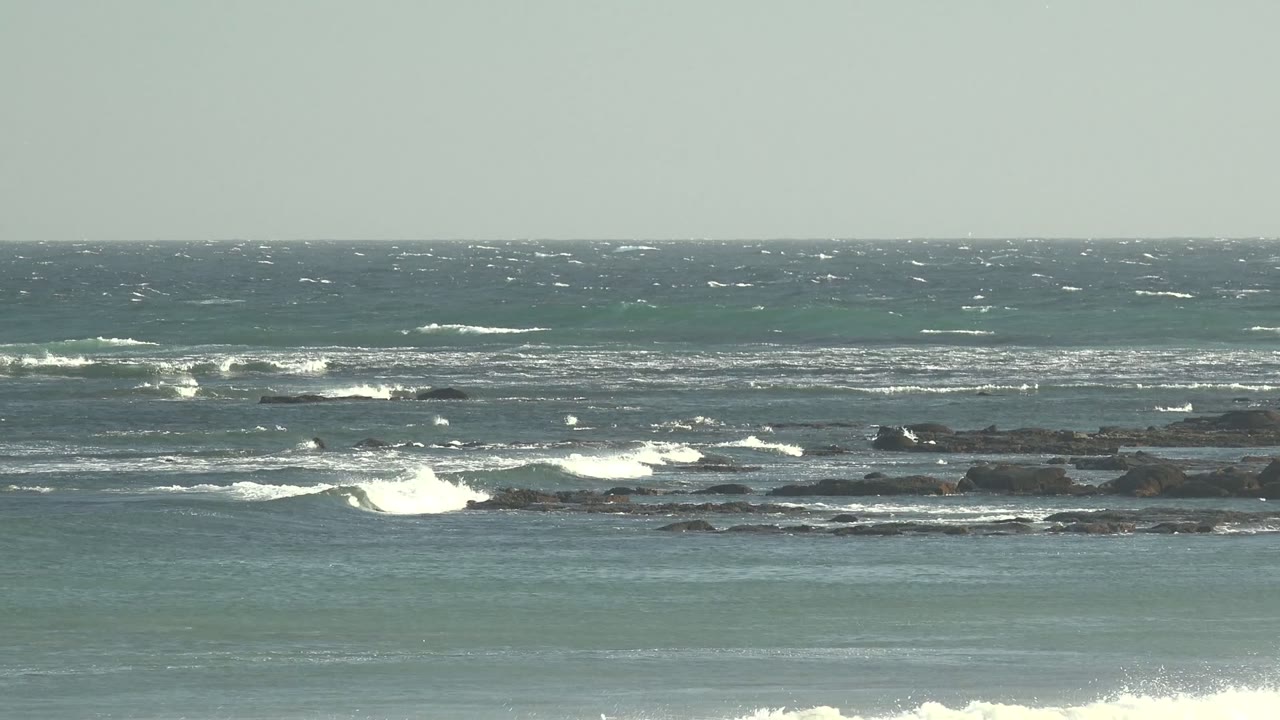White surf rolling across low rocks under a pale horizon