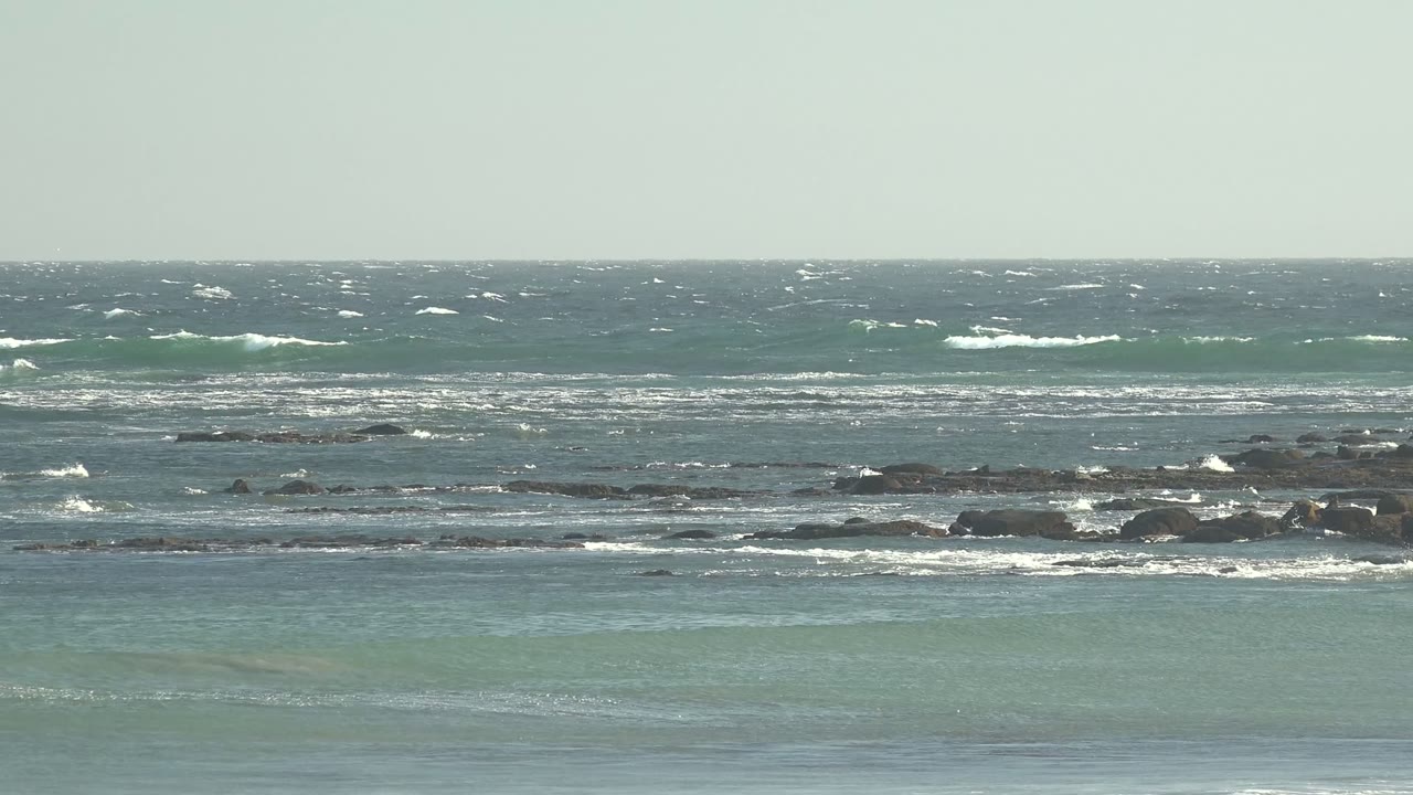 White surf rolling across rocks in blue-green coastal water