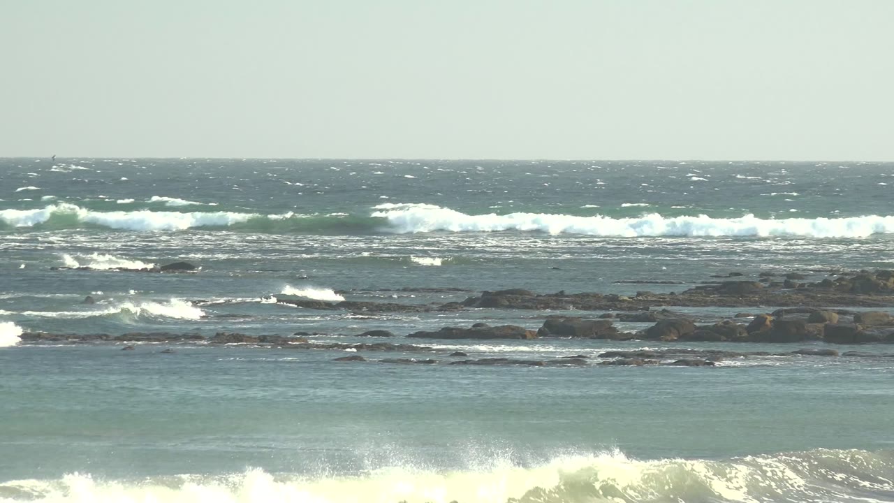 White surf lines crossing dark rocks under a pale sky