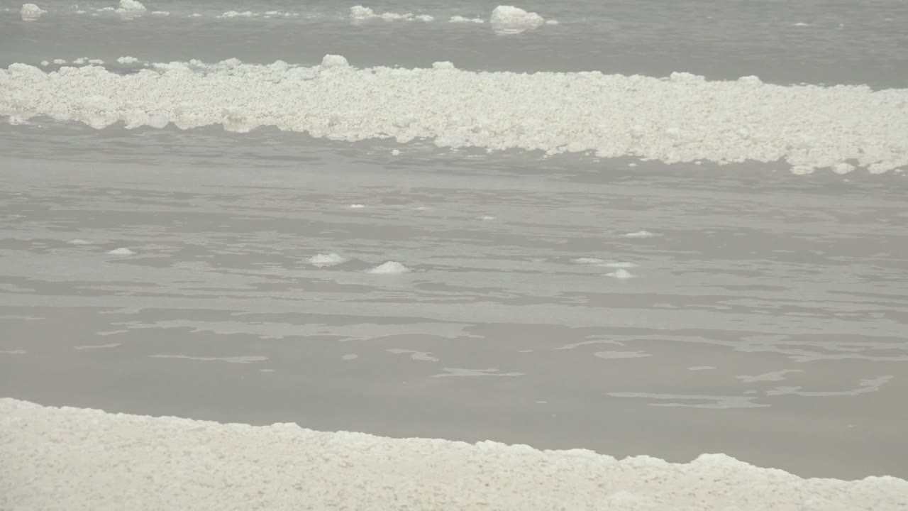 Close view of white salt crystal ridges crossing shallow gray water in Guerrero Negro, Baja California Sur, Mexico, with no visible people.