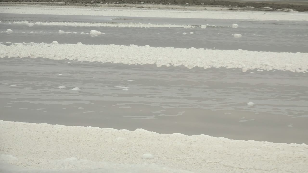 A broader view shows parallel white salt crystal rows separated by gray water channels in Guerrero Negro, Baja California Sur, Mexico, with no visible people.