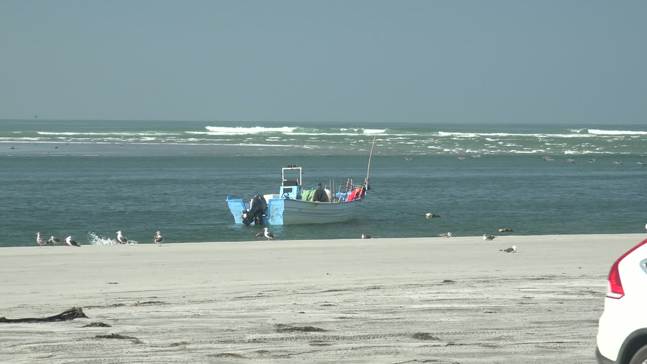 Small blue boat beside ocean waves on a sandy beach.