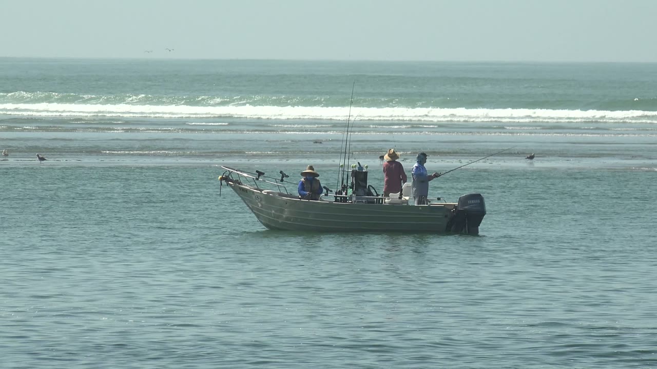 People stand and sit in a small fishing boat near surf.
