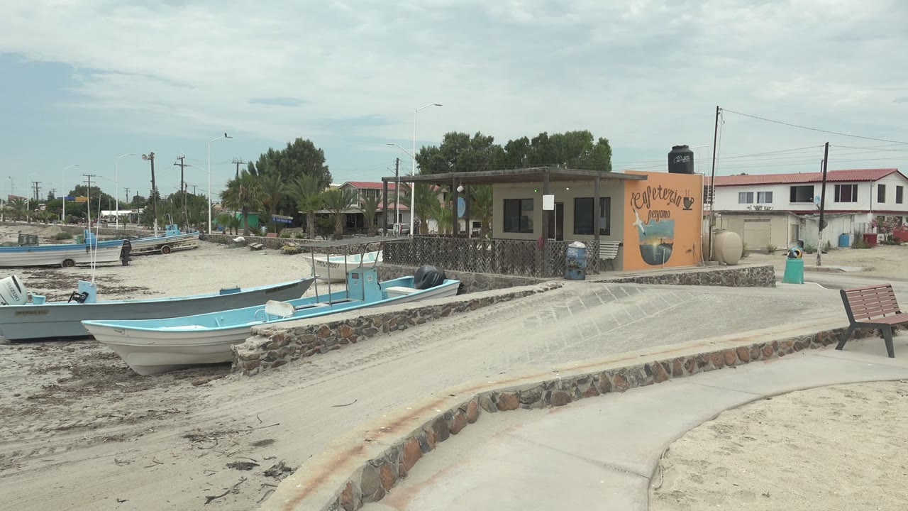 Small boats on a sandy shore beside a building with a cafeteria sign.
