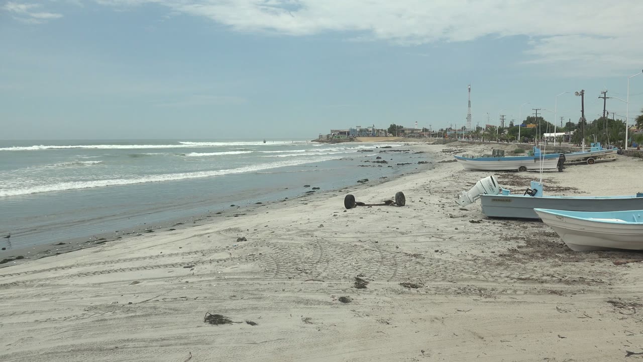 Open sandy shore with small boats, rolling waves, and no visible people.