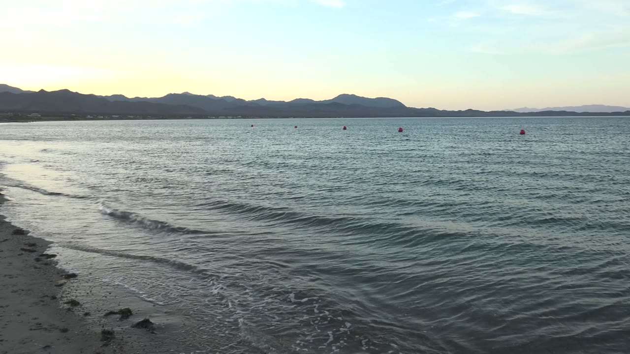 Low waves ripple across shallow water toward a sandy shoreline.