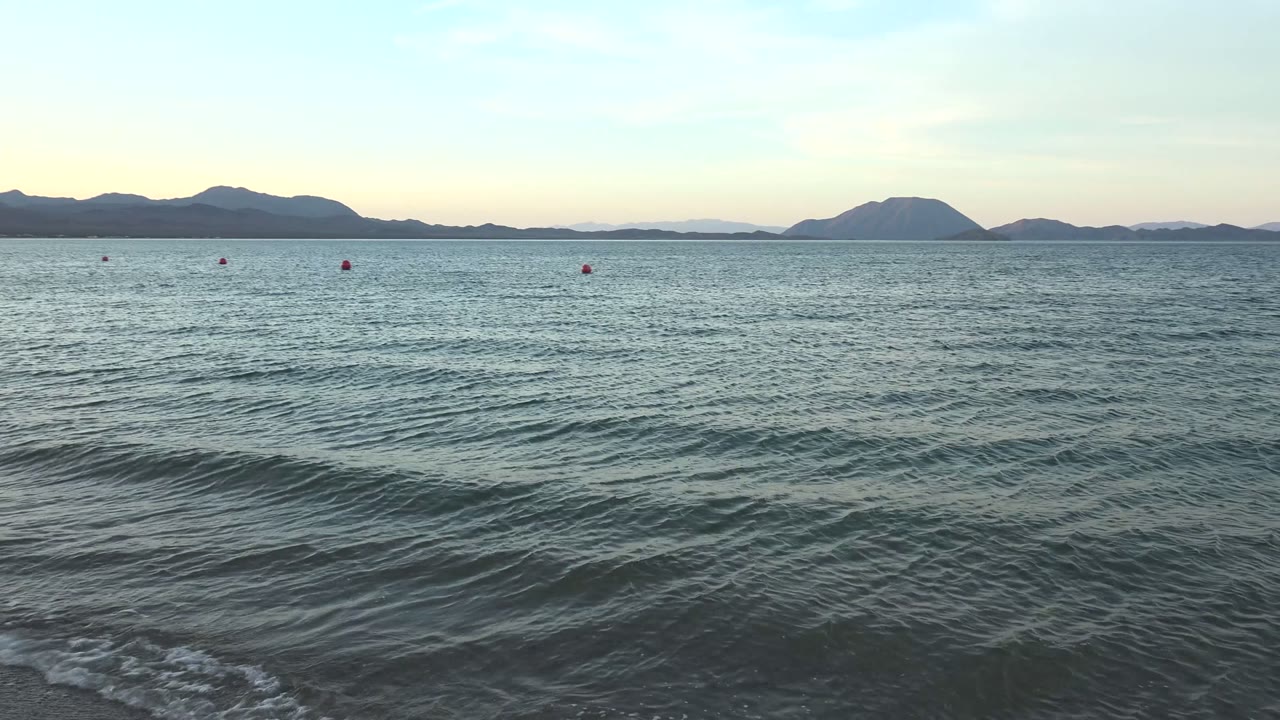 Rippling sea surface with red buoys and distant islands.