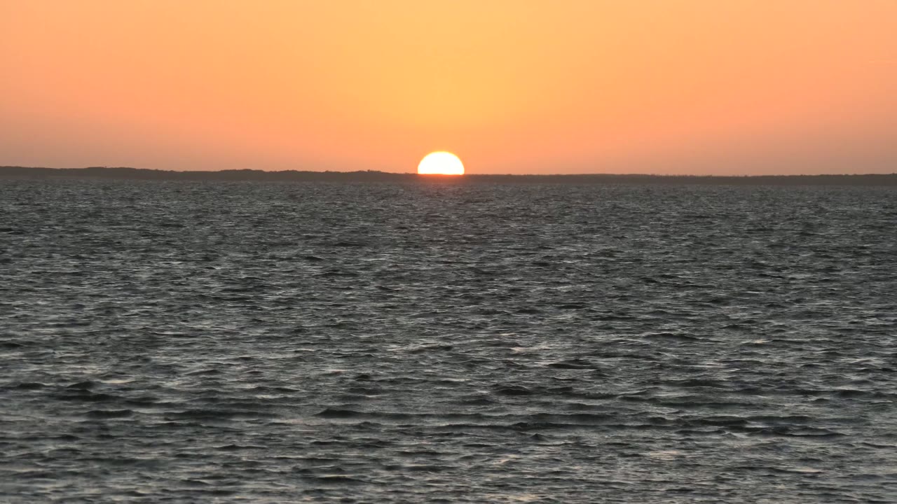 Sunset disk near the horizon above textured sea