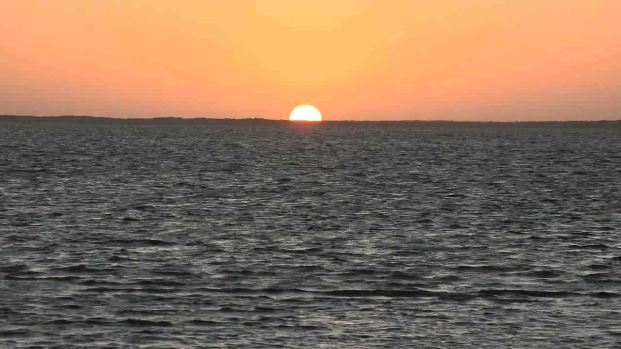 The sun remains low against the far horizon while darker ocean ripples occupy the foreground in San Carlos, Baja California Sur, with no visible people.