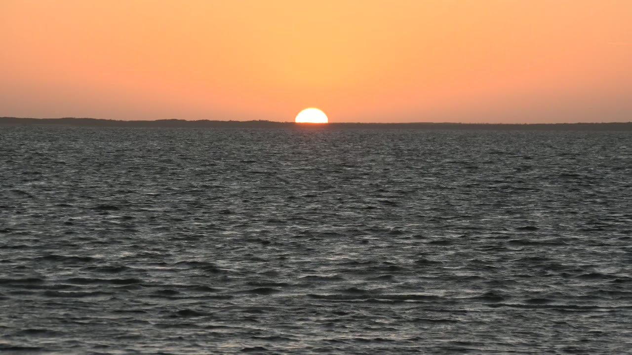 Sunset disk just above the distant ocean horizon