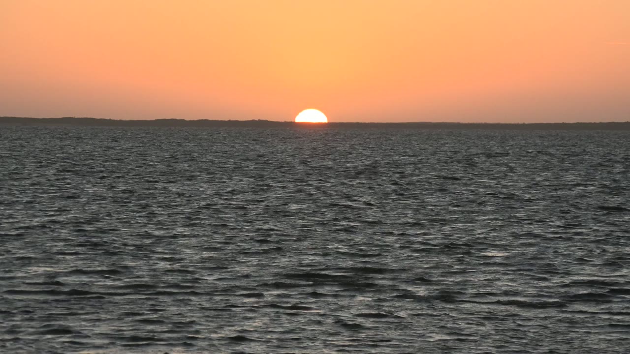 Low sun touching the horizon above dark ocean waves.
