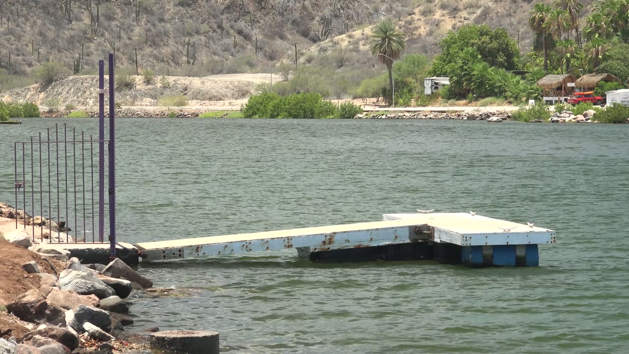 Floating dock on rippling water with a red vehicle near the far trees.