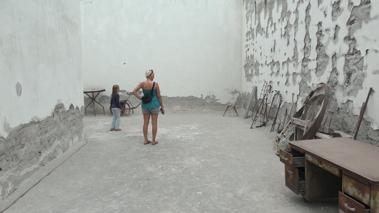 Child near a wheelbarrow while a woman watches in a concrete courtyard.